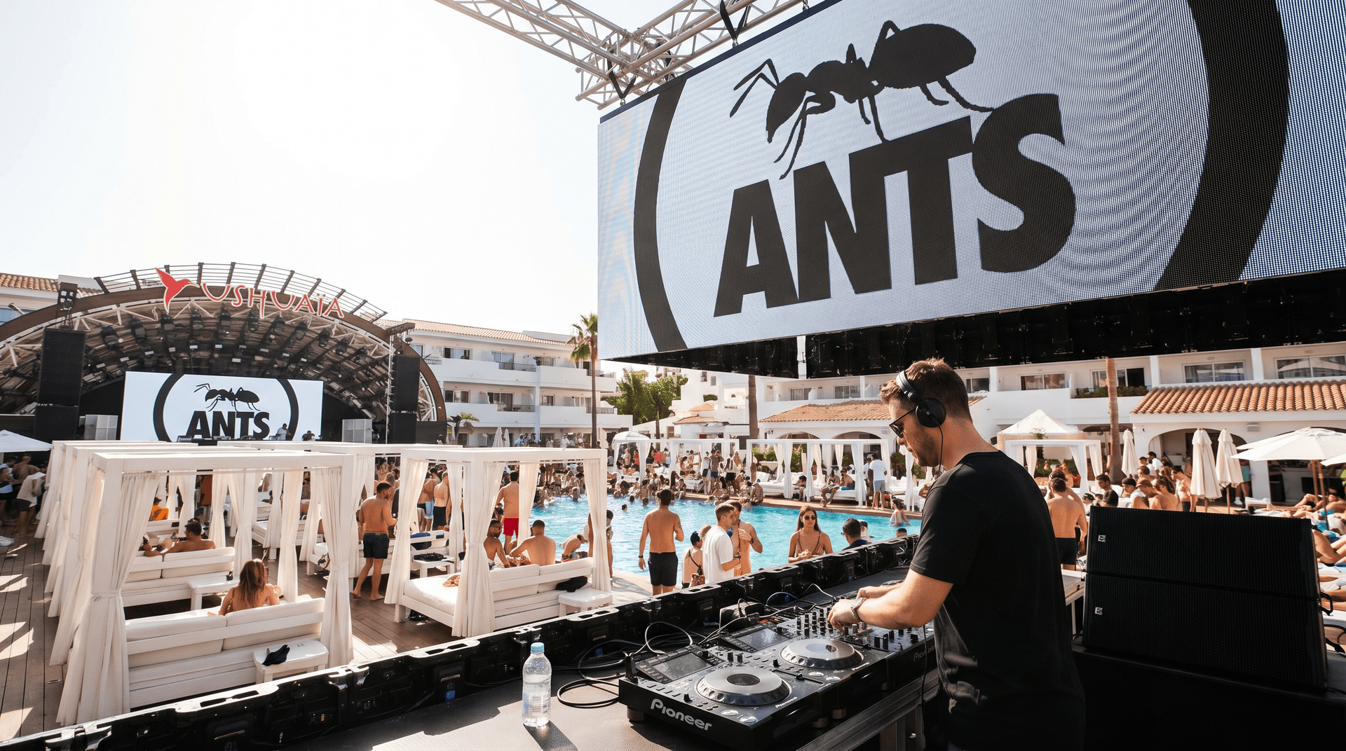 ANTS underground techno party brand logo displayed on outdoor venue screens at Ushuaïa Ibiza with DJ booth