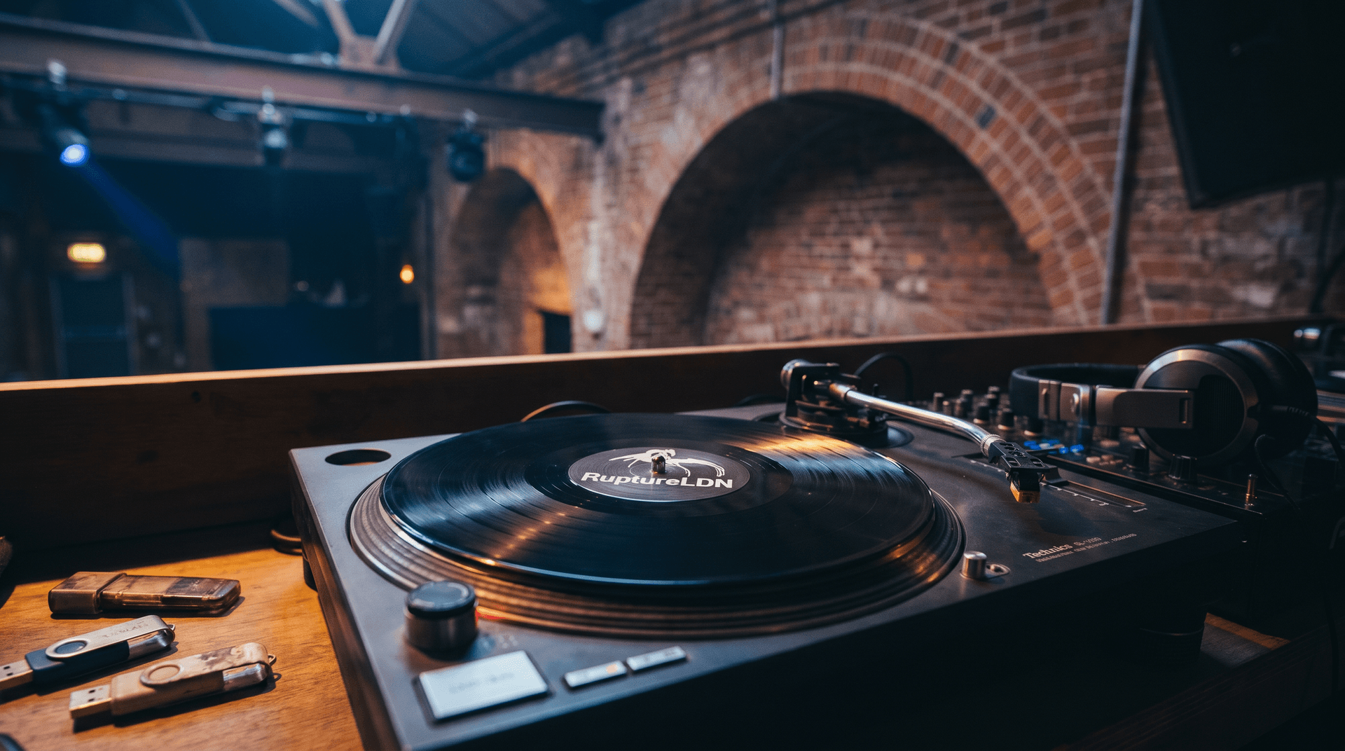 Vinyl record on turntable with Corsica Studios architectural elements and RuptureLDN branding in background