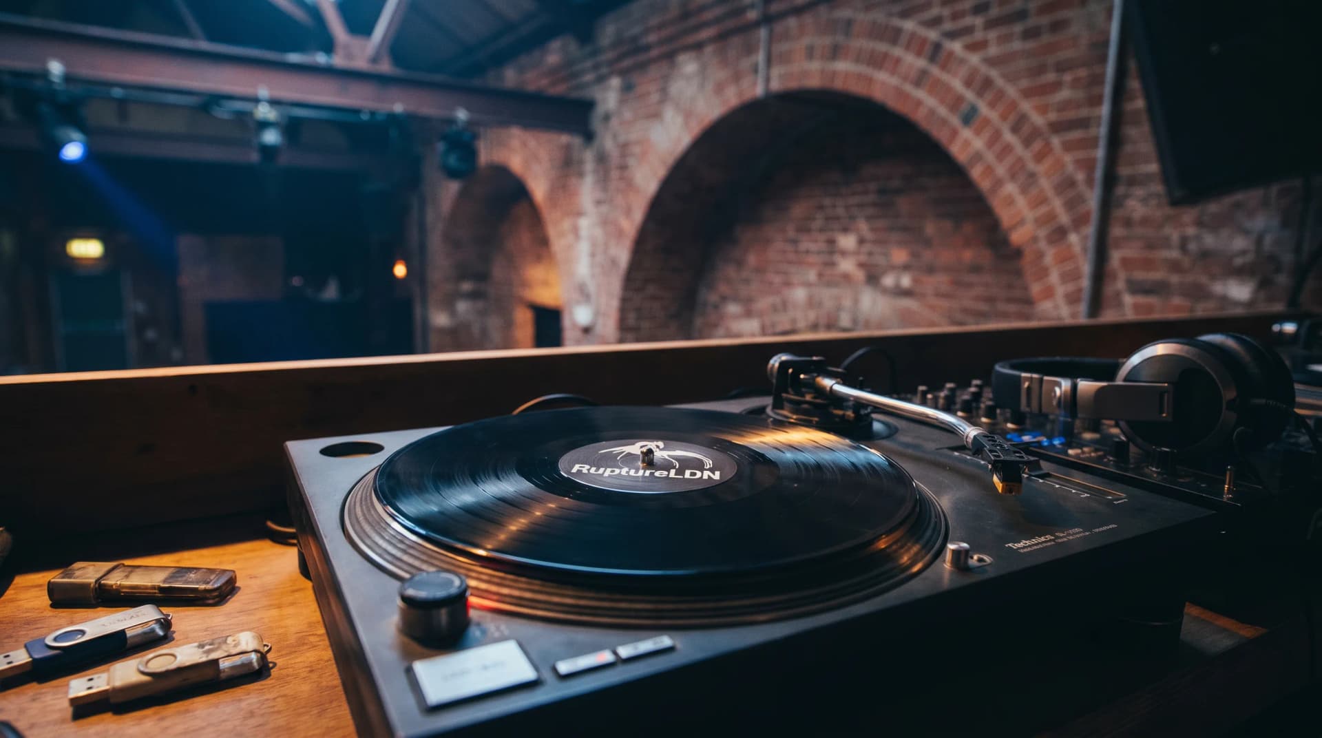 Vinyl record on turntable with Corsica Studios architectural elements and RuptureLDN branding in background