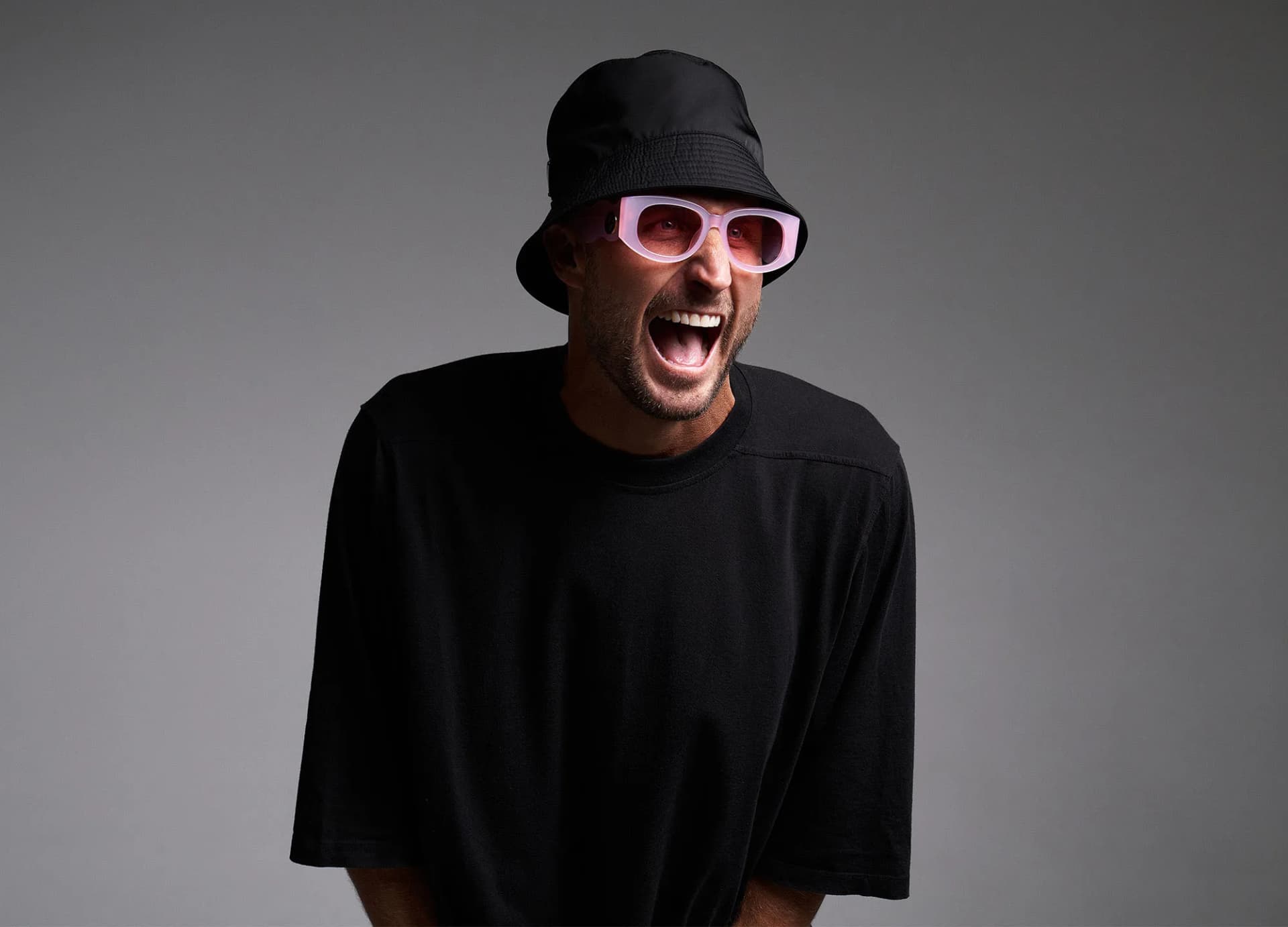 FISHER wearing a black bucket hat and pink sunglasses against a grey backdrop