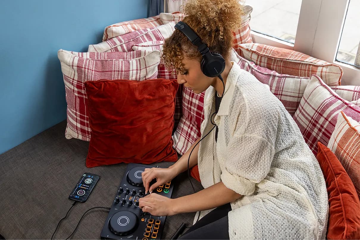 A DJ on a sofa mixing on an AlphaTheta DDJ-FLX2 connected to a phone