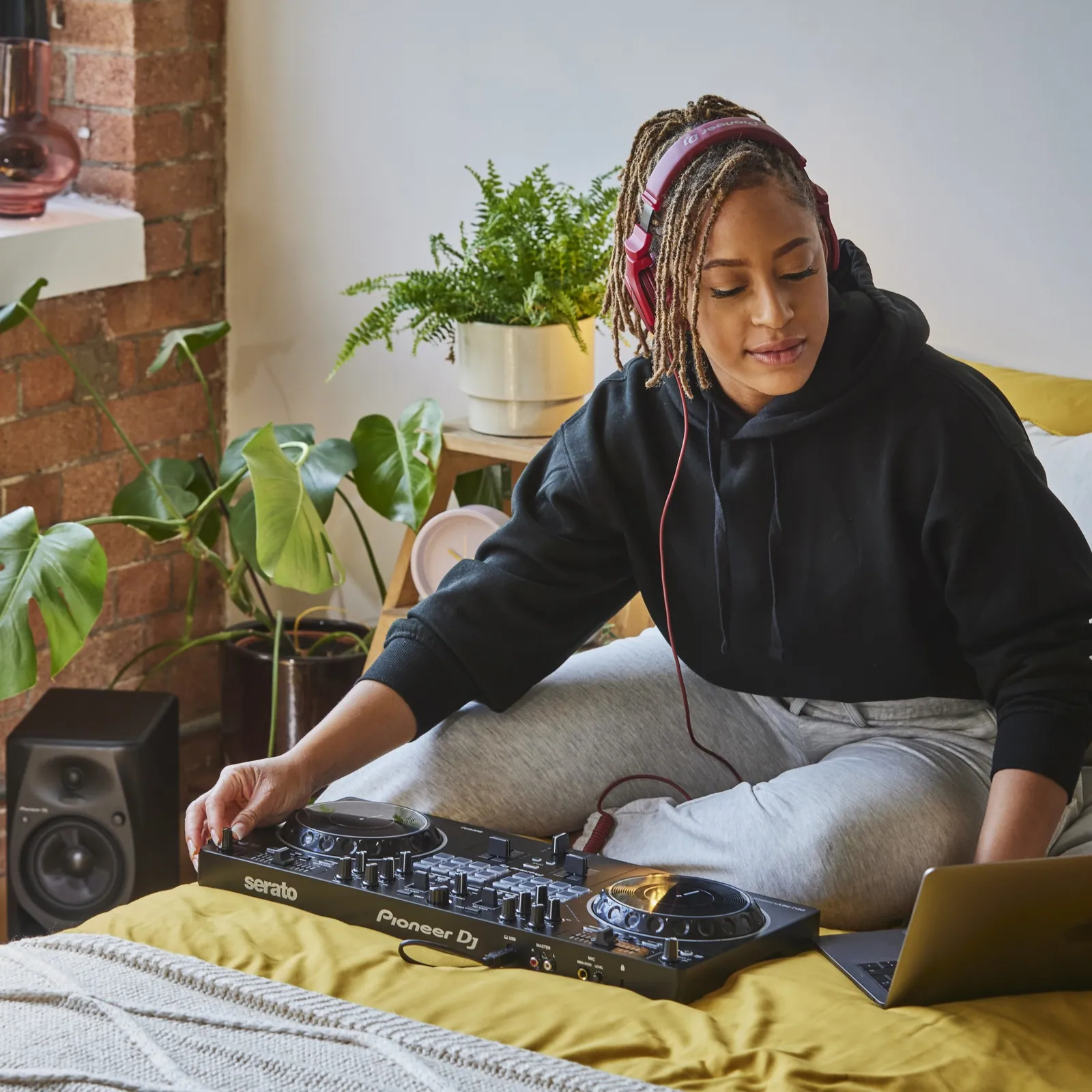 A DJ playing a Pioneer DJ DDJ-REV1 on a bed beside a laptop