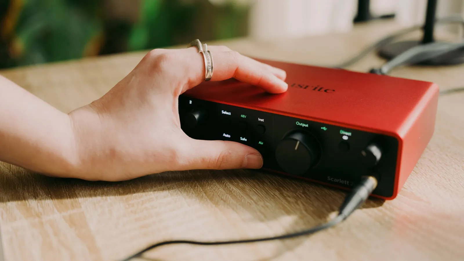 A hand on a Focusrite Scarlett 2i2 (4th Gen) on a wooden desk