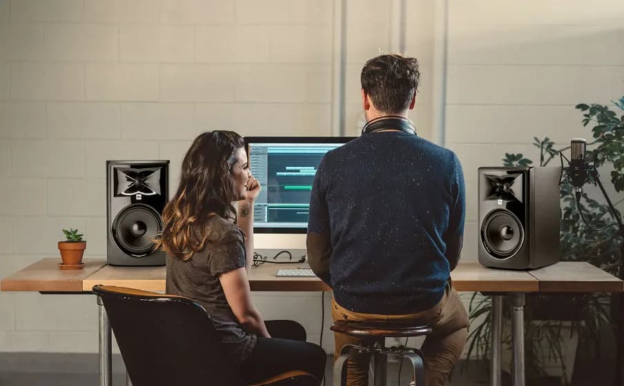 Two people at a studio desk with JBL 3 Series MkII monitors either side of the screen