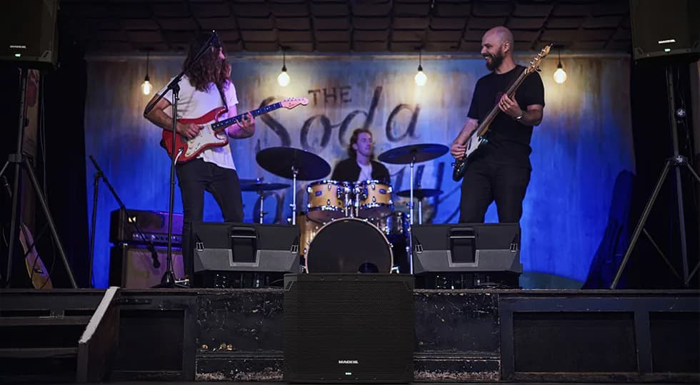 A band on a small stage with a Mackie Thump18Sv4 at the front