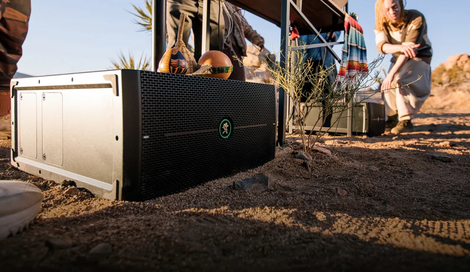 A Mackie ThumpSub GO lying flat on sandy ground at an outdoor gathering