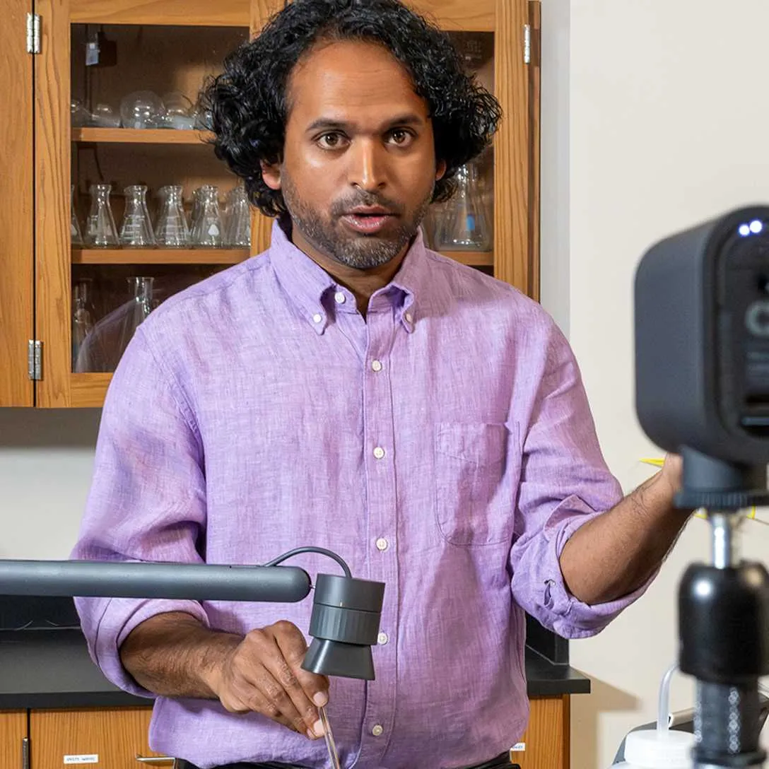 A presenter beside a Mevo Start on a stand