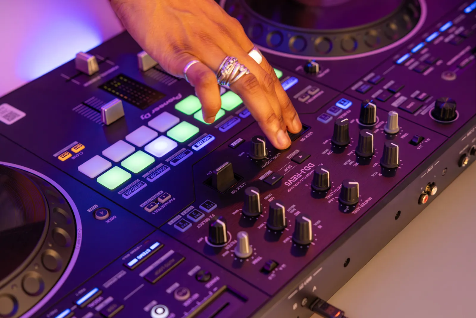 A hand on the Performance Pads and mixer knobs of the Pioneer DJ DDJ-REV5
