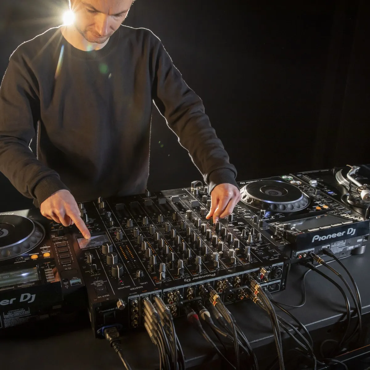 A DJ adjusting a Pioneer DJ DJM-V10 between two CDJ-2000NXS2 players