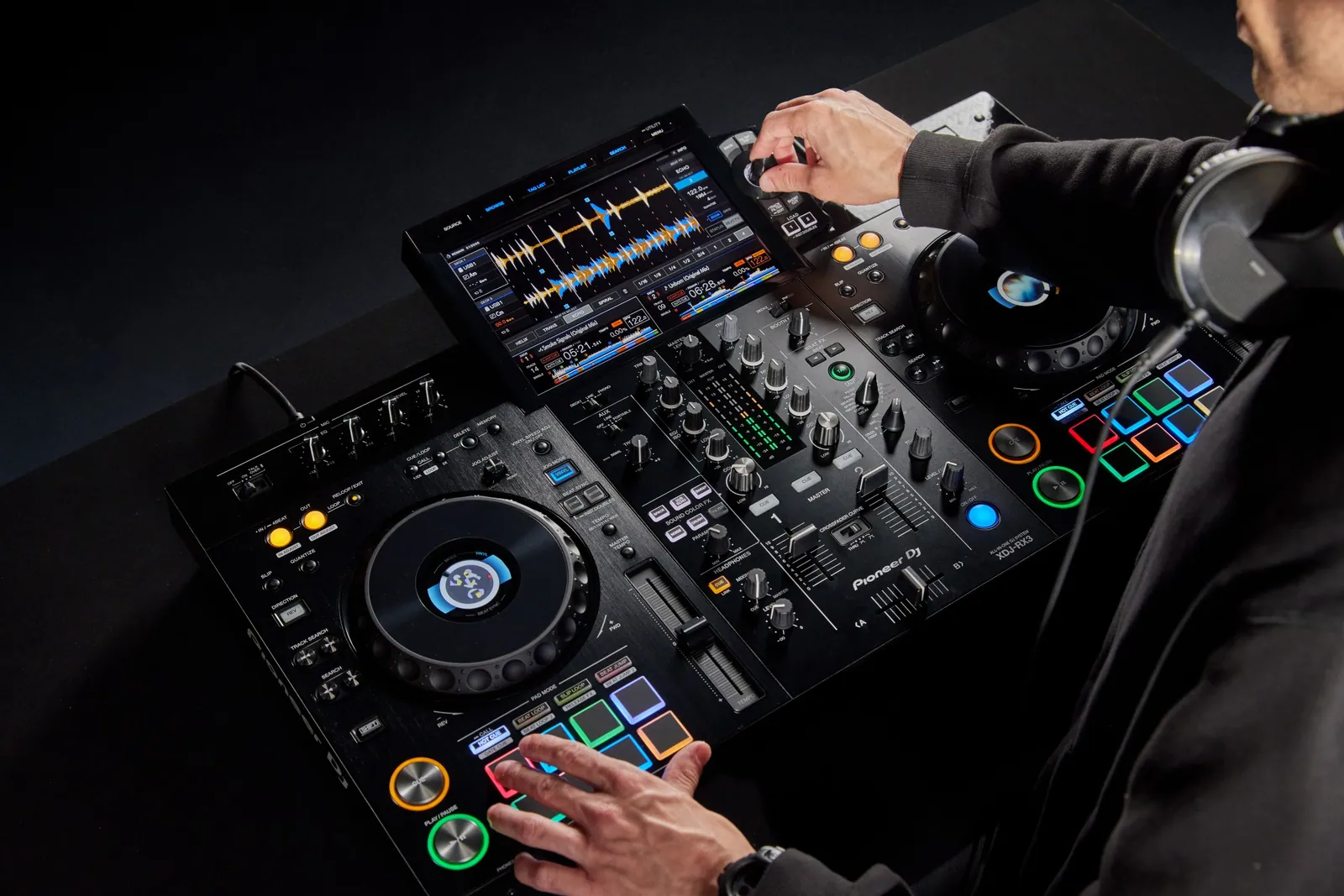 A DJ's hands on the touch screen and pads of a Pioneer DJ XDJ-RX3