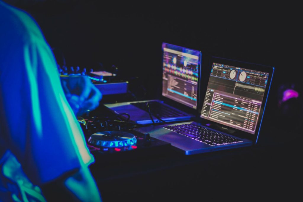 Two laptops displaying different DJ playlists